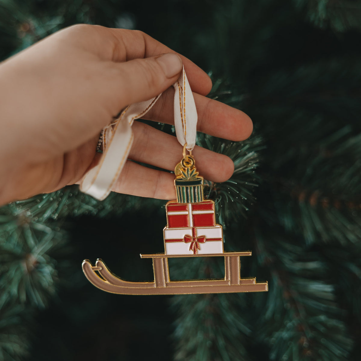 Goldener Schlitten-Baumschmuck am Band, mit gestapelten Geschenkboxen und Schleife