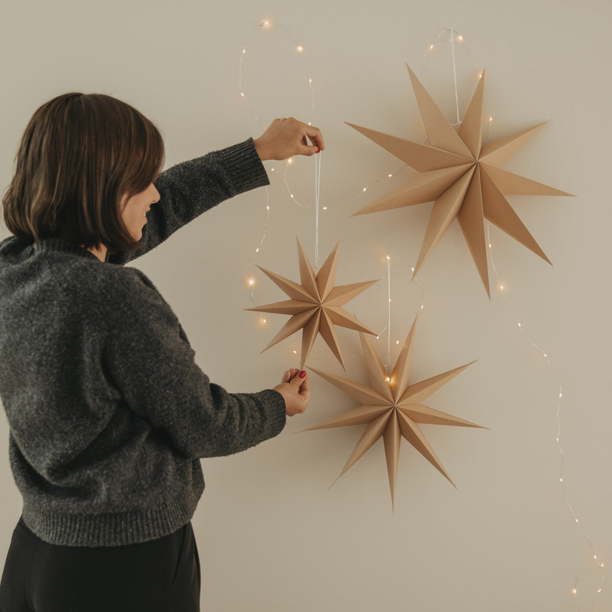 Braunes Papierstern-Set: Person befestigt mehrere braune Sterne an der Wand