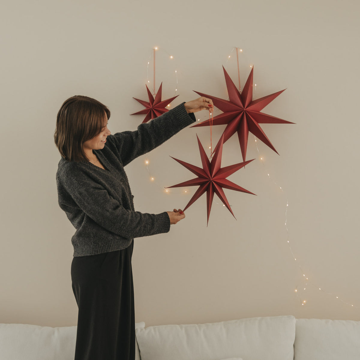 Rote Papiersterne im 3er-Set an der Wand, mehrere Sterne mit Lichterfäden