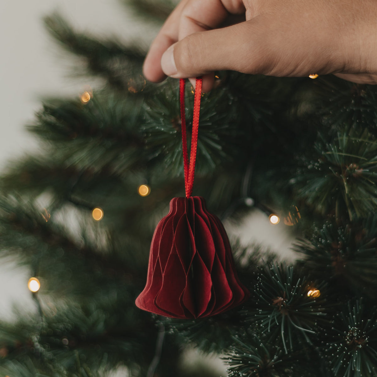 Roter Papier-Glockenanhänger mit Falten, von Hand am Weihnachtsbaum aufgehängt
