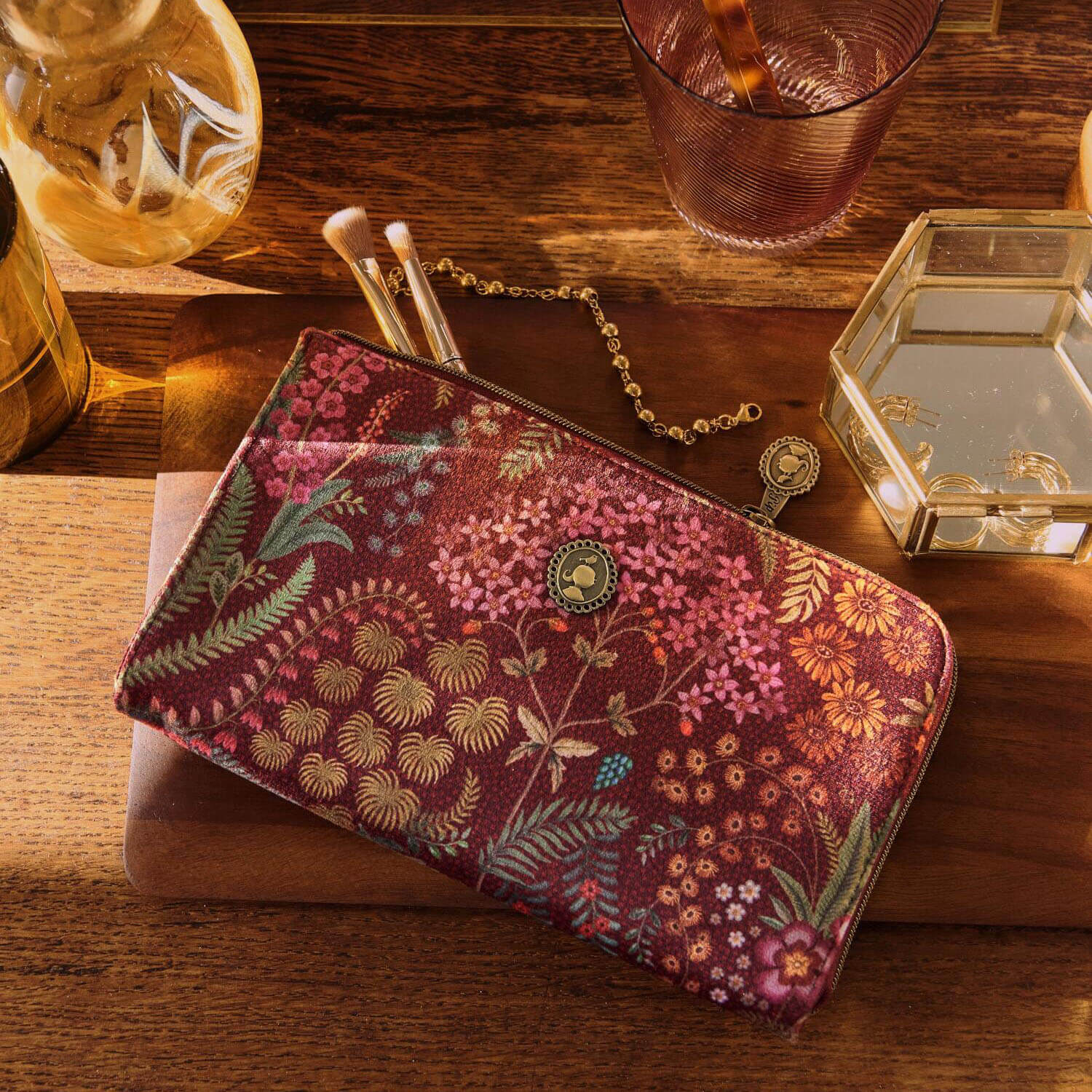 Kosmetiktasche mit Reißverschluss, bordeauxfarbenem Floral-Print und runder Metallplakette.
