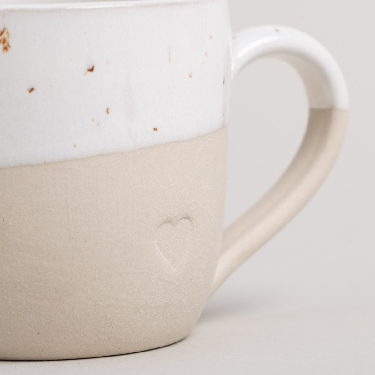 Nahaufnahme Espressotasse: Herzrelief auf beigem Korpus, weißer Rand, Henkel