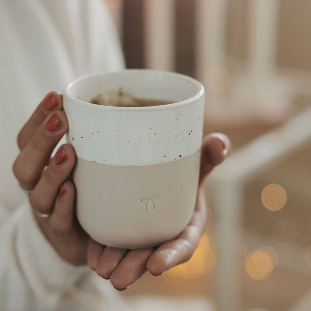 Becher mit warmem Getränk, weißem Rand und Schleifen-Emblem auf Naturton