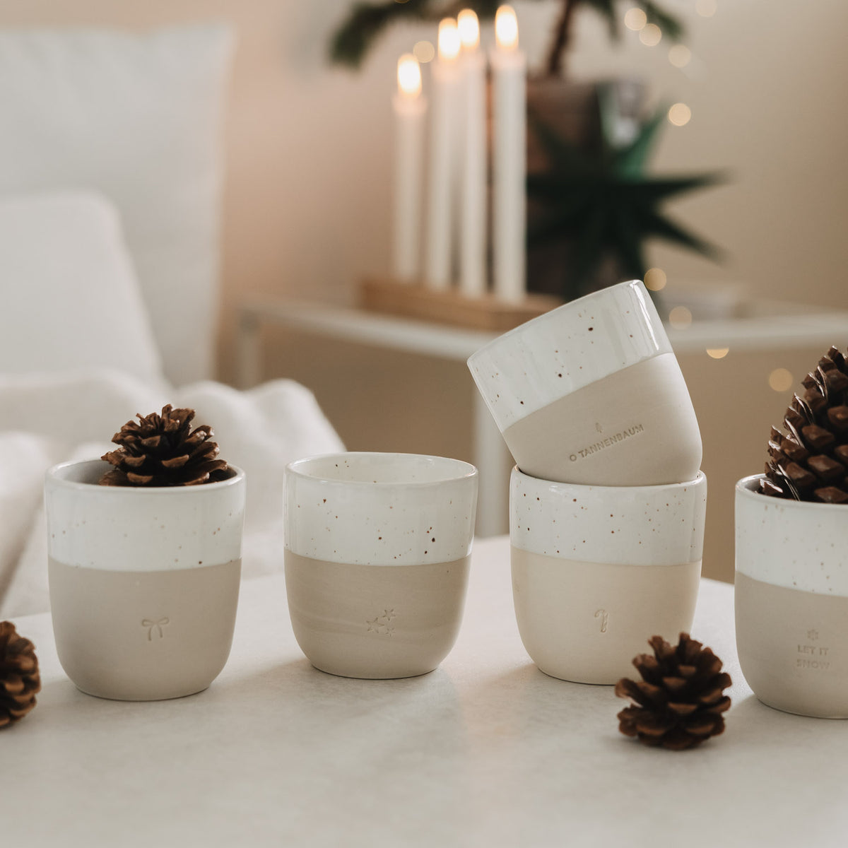 Mehrere Becher mit weißem Streifen, Sprenkeln und Schleifen-Emblem auf Naturton