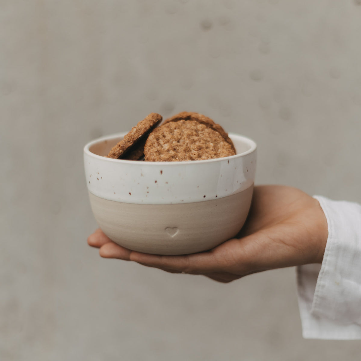 Herz-Schüssel mit Sprenkeln, weiß/cremefarben, von einer Hand gehalten