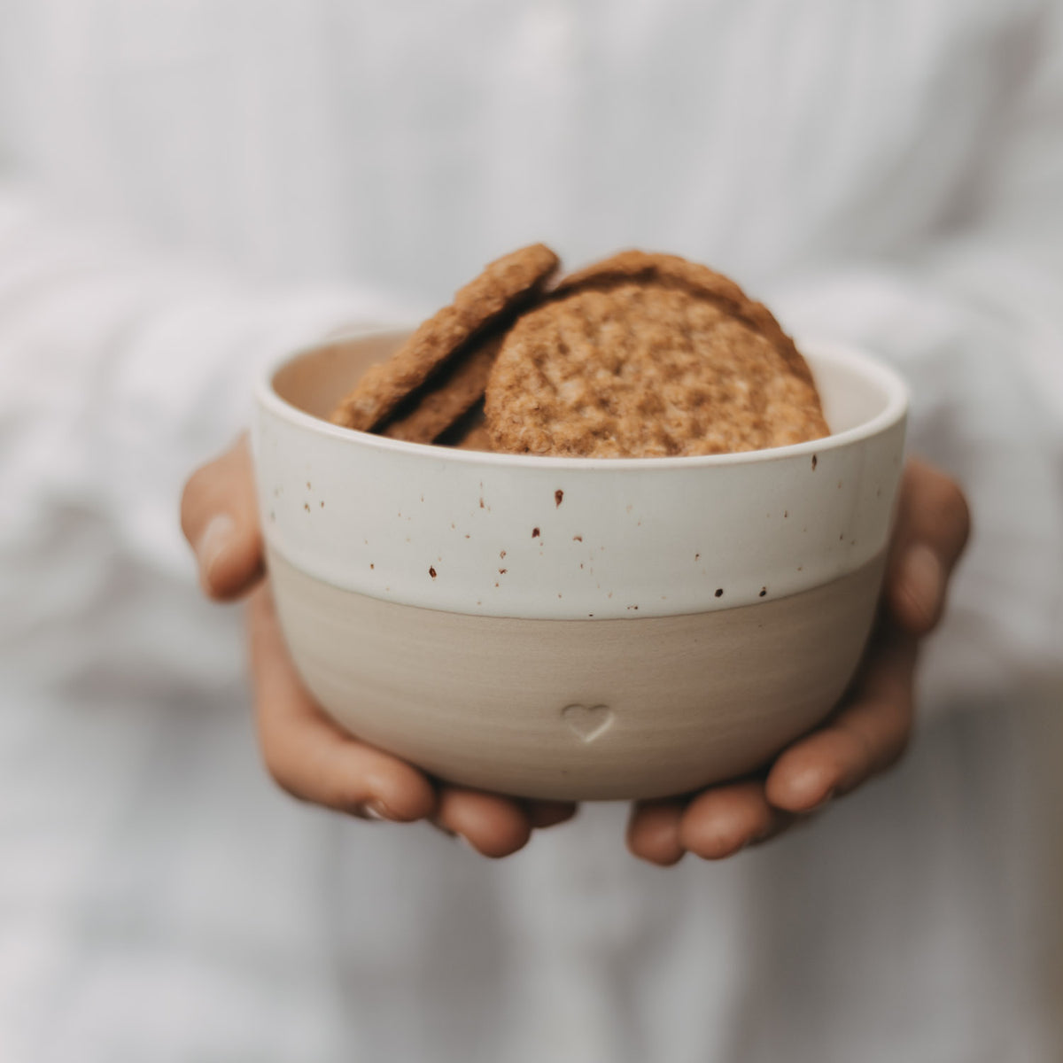 Herz-Schüssel mit Sprenkeln, weiß/cremefarben, gefüllt mit Keksen, von Händen gehalten