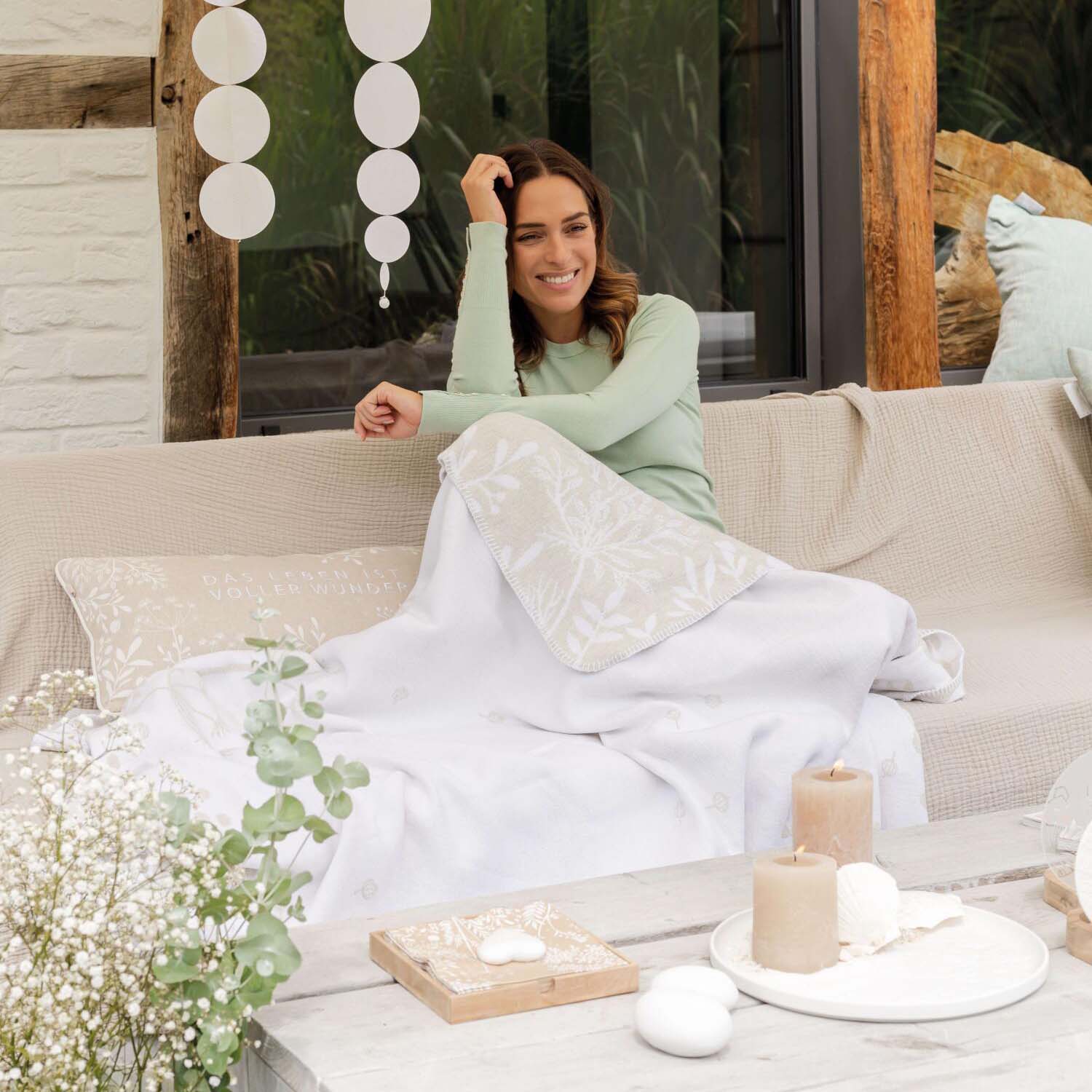 Rechteckiges Kissen in Weiß/Beige mit weißem Pflanzenmuster und hellen Schriftzügen