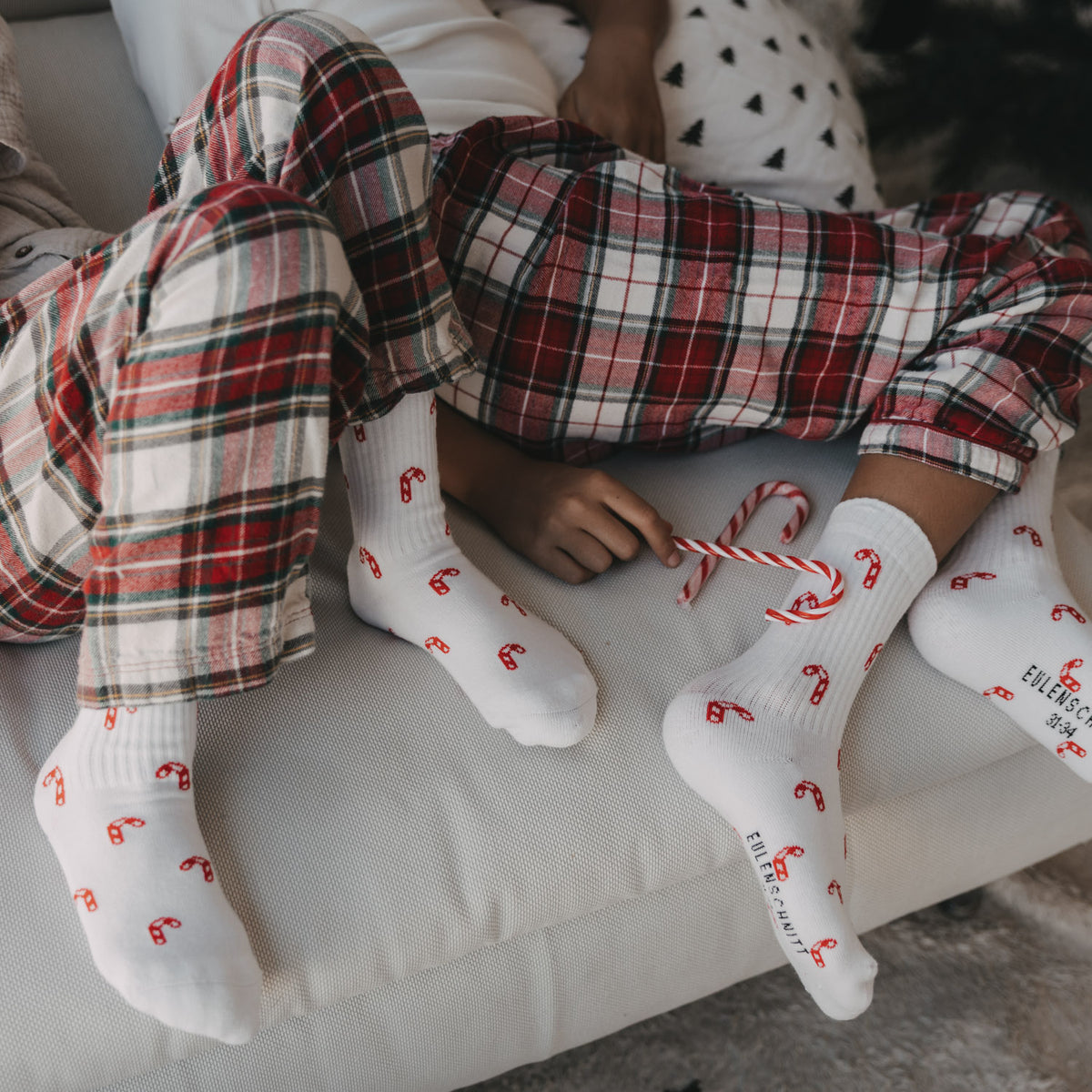 Weiße Kinder-Socken mit rotem Zuckerstangen-Allovermuster, Sockenpaar im Sitzen