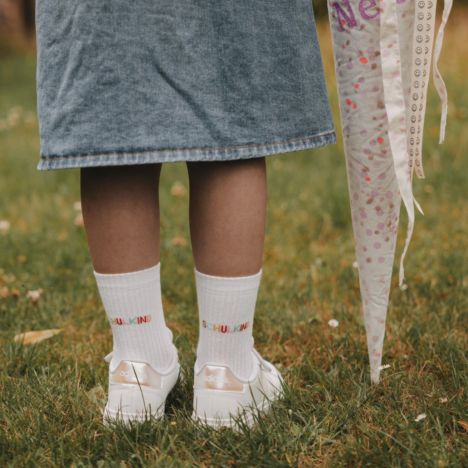 Weiße Kindersocken mit „Schulkind“-Schrift, getragen zu weißen Sneakern