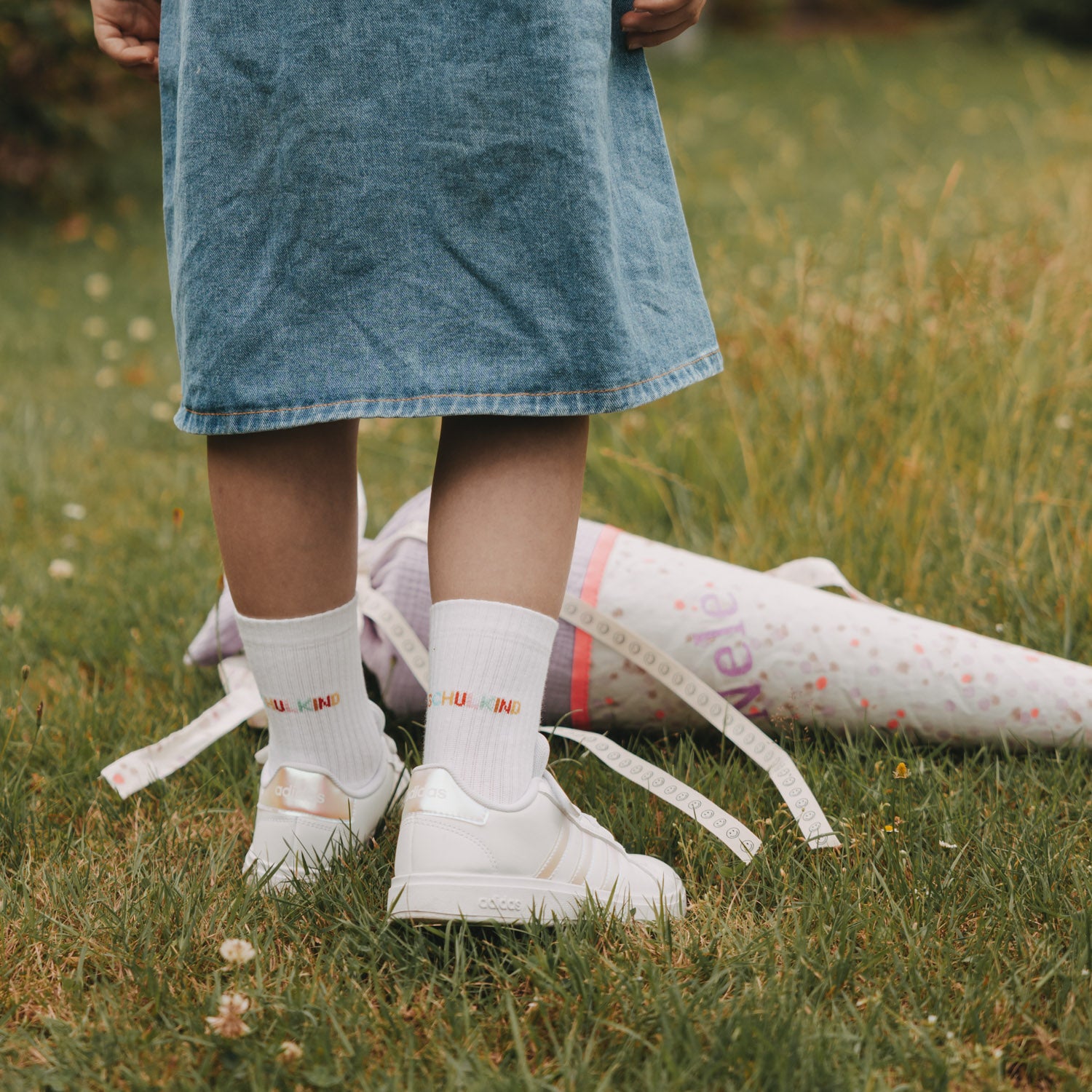 Weiße Kindersocken mit „Schulkind“-Aufdruck am Knöchel, mit weißen Sneakern im Gras