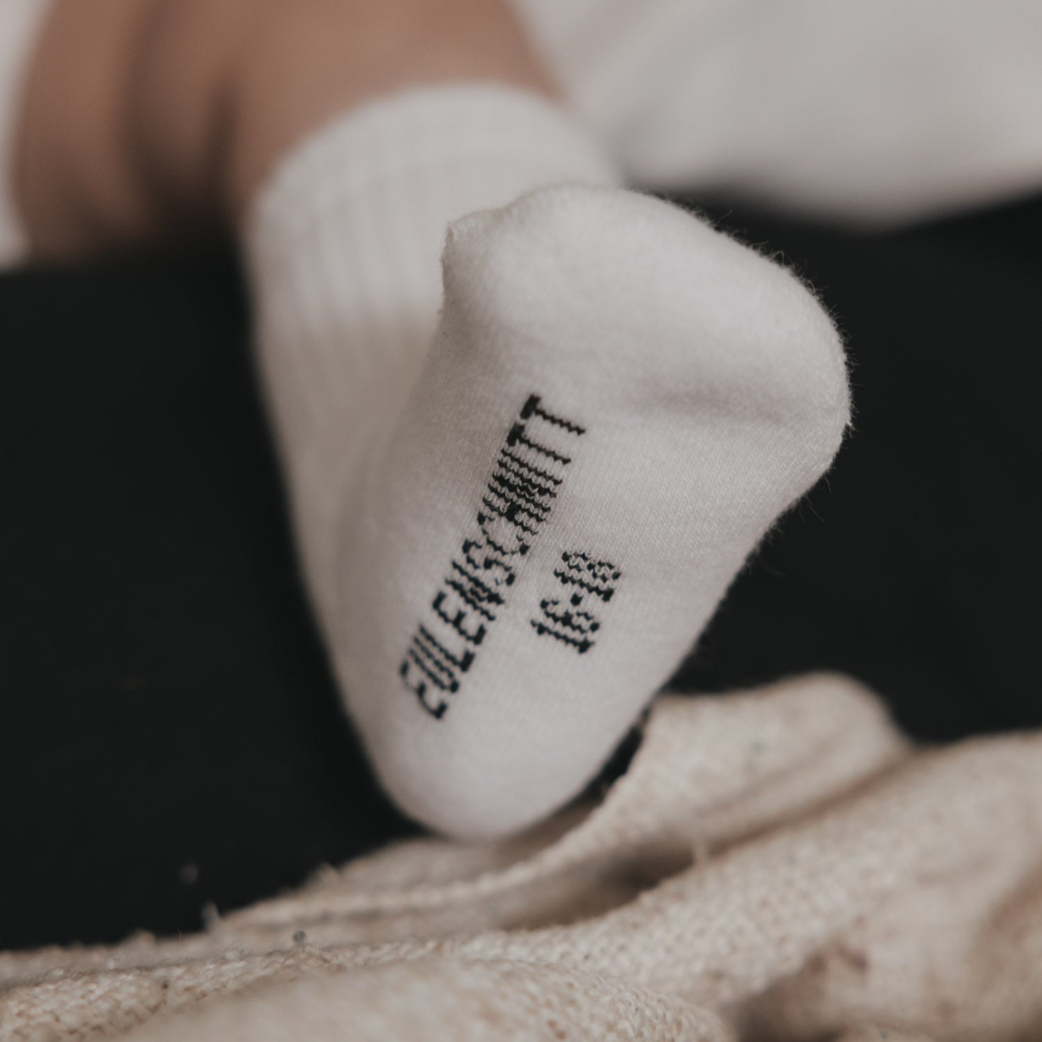 Weiße Babysocke mit Zehenpartie und Schriftprint am Fuß
