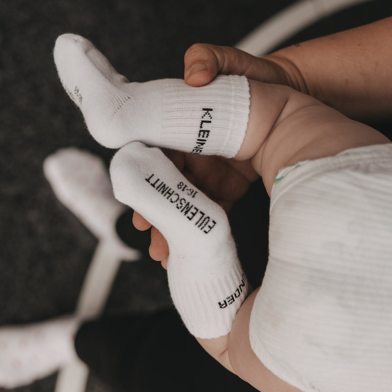 Weiße Babysocke mit Fersenaufdruck und eingestrickter Schrift am Fuß