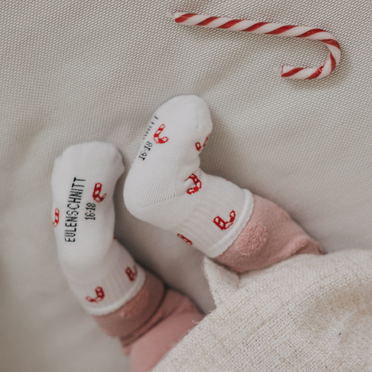Babysocken in Weiß mit rotem Zuckerstangenmuster, Vorderseite und Ferse im Detail