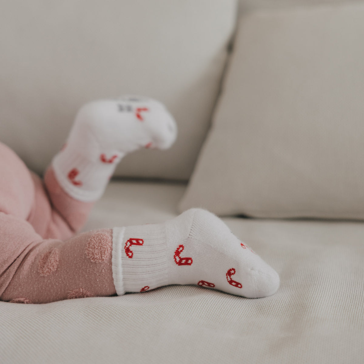 Babysockenpaar in Weiß mit rotem Zuckerstangen-Allover, angelehnt im Sitzbereich