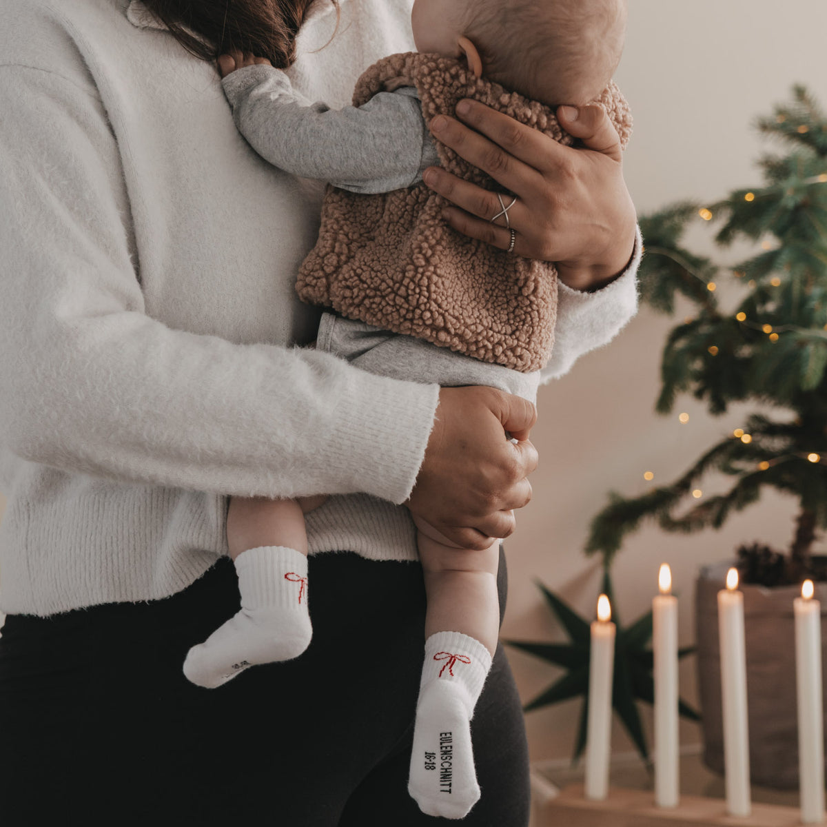Babysocken in Weiß mit roter Schleife, zwei Socken sichtbar am Fuß des Kindes