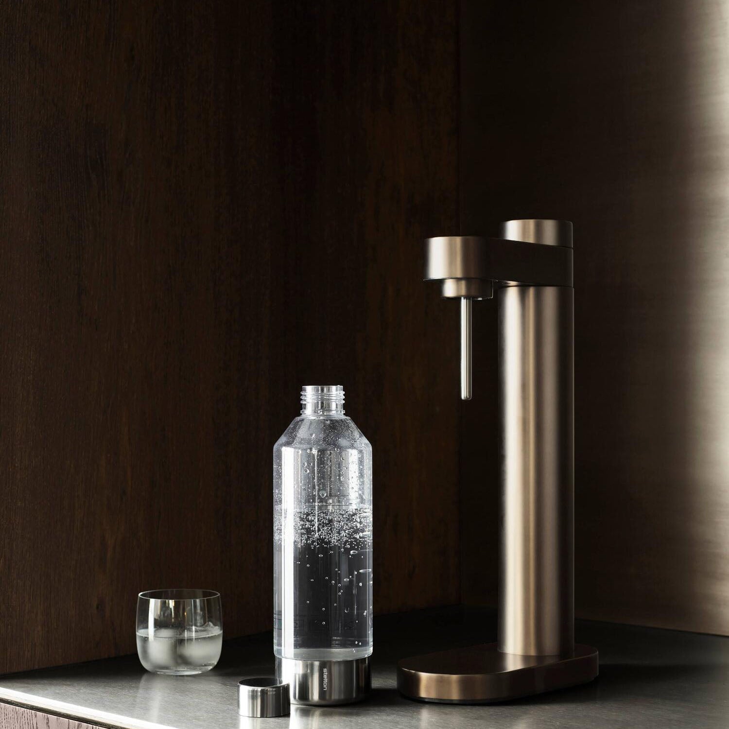 Wassersprudler auf Sockel mit Glasflasche, kleinem Becher und Metallrohr