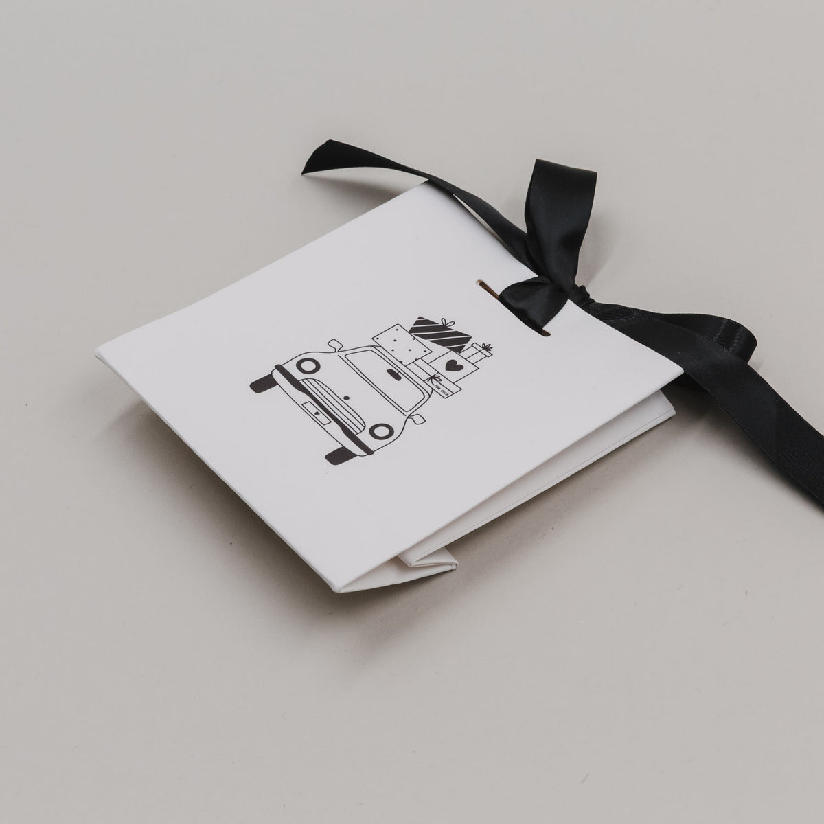 Weiße Mini-Geschenktüte aufgestapelt mit schwarzer Schleife und Auto-Illustration