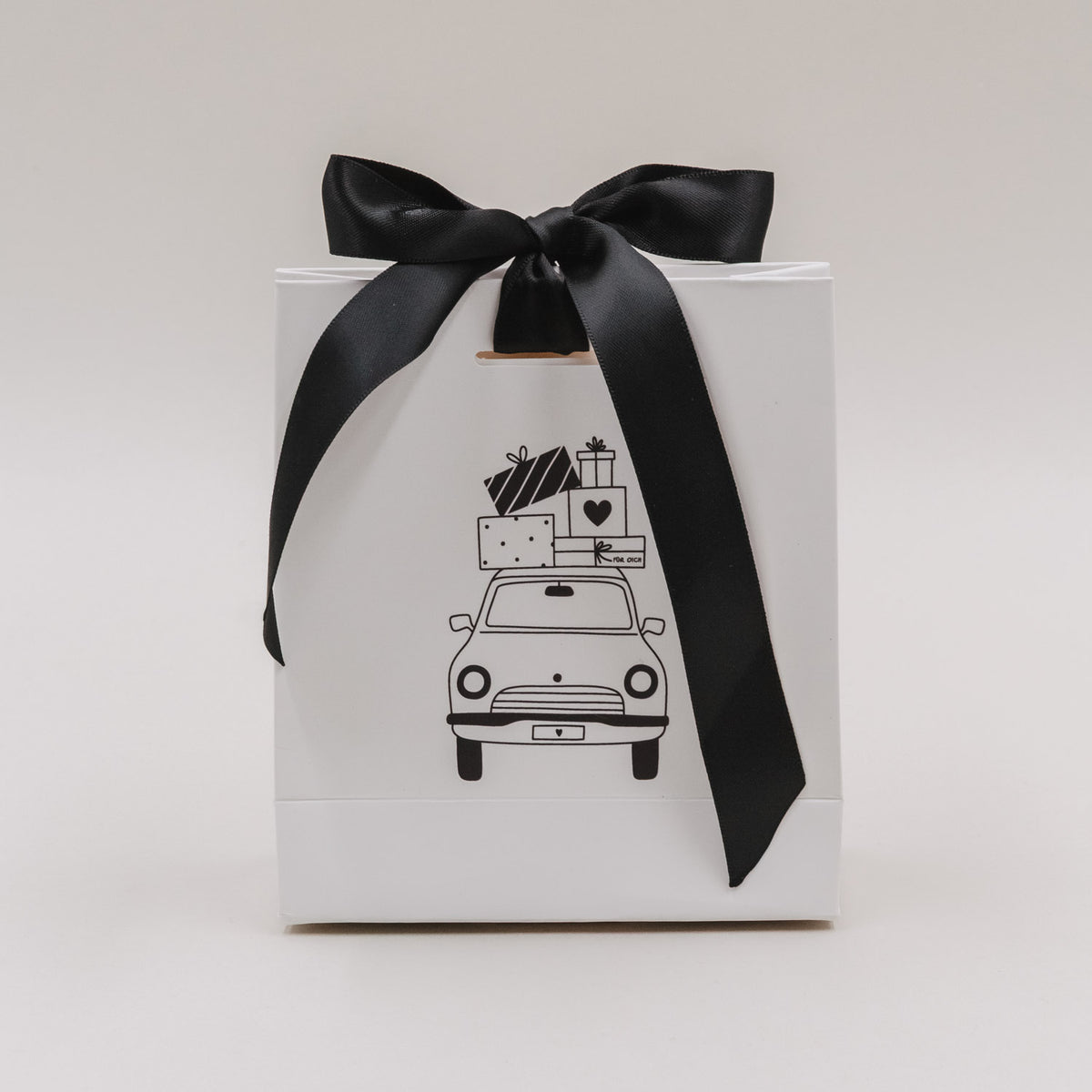 Weiße Geschenktüte mit schwarzer Schleife und Weihnachtsauto-Motiv, frontale Ansicht