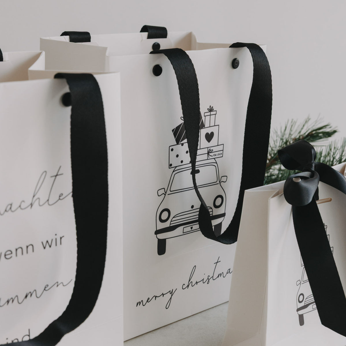 Nahansicht mehrerer weißer Geschenktüten mit schwarzem Trageband und Weihnachtsauto-Print.