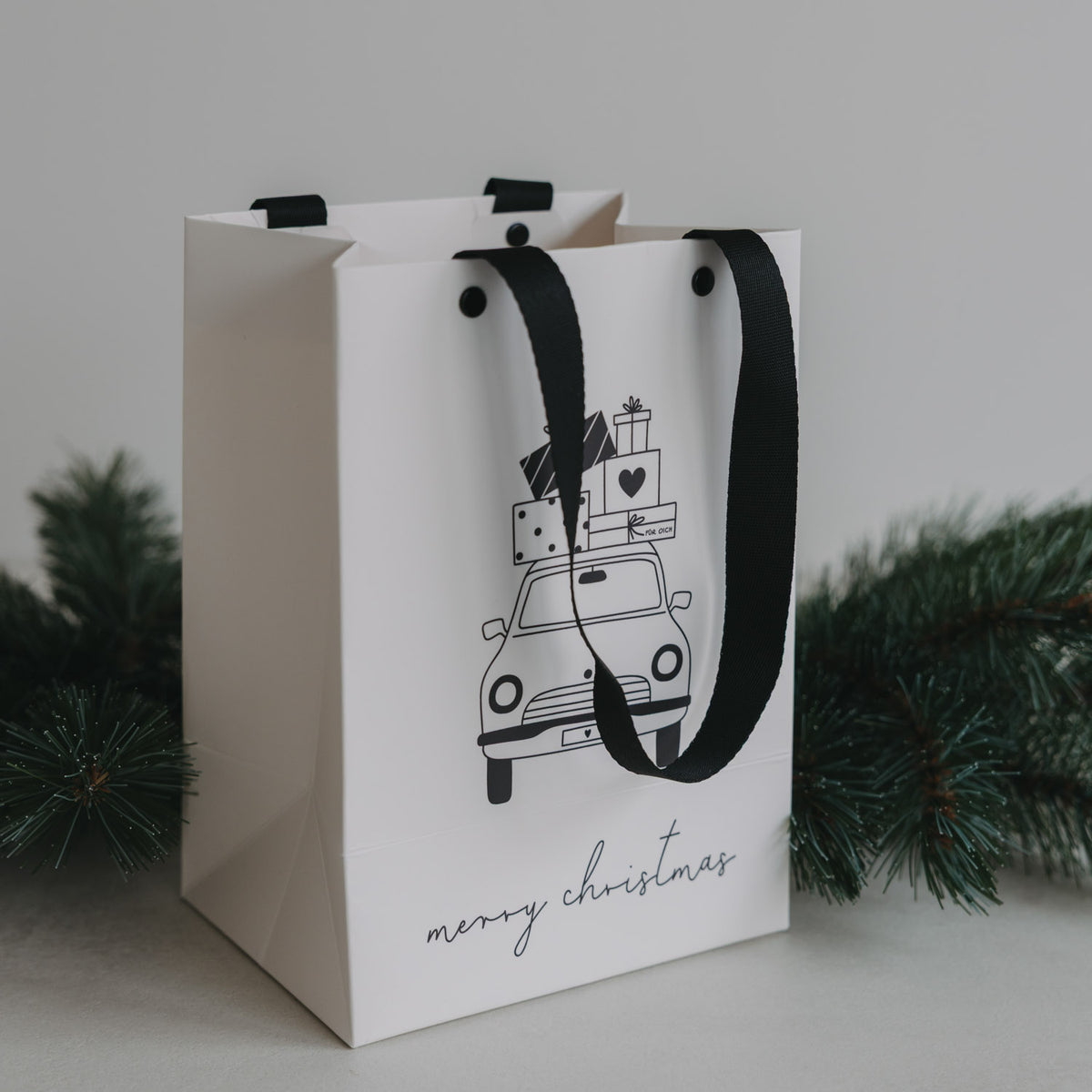 Weiße Geschenktüten im 2er-Set mit schwarzem Trageband und Weihnachtsauto-Motiv, „merry christmas“.