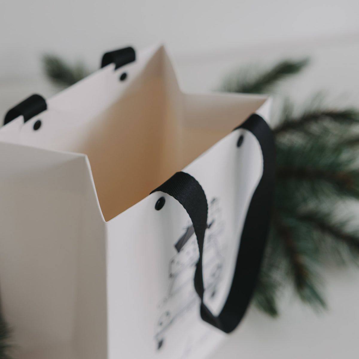 Weiße Geschenktüte, seitlich nah; schwarzes Trageband über Weihnachtsauto-Illustration.
