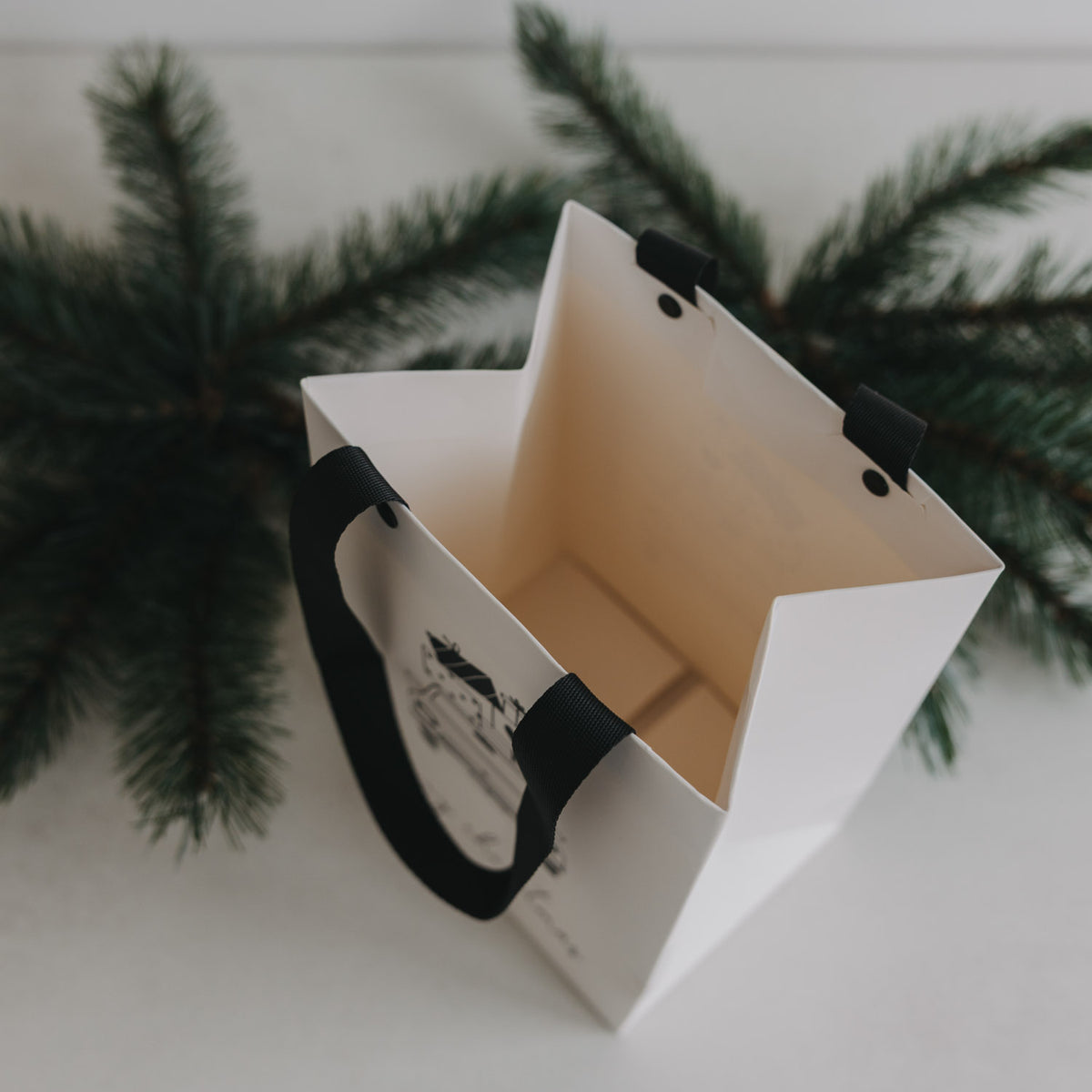 Weiße Geschenktüte mit schwarzem Trageband, innen geöffnet; Weihnachtsauto-Motiv sichtbar.
