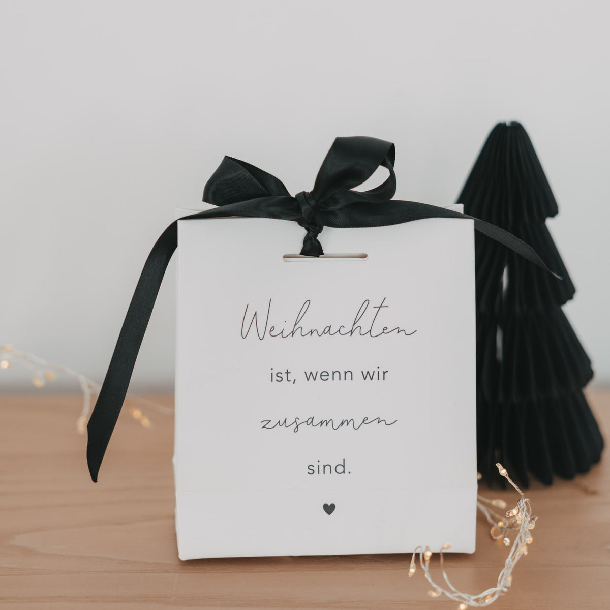 Weiße Geschenktüte mit schwarzem Schleifenband und Aufdruck „Weihnachten ist, wenn wir zusammen sind.“