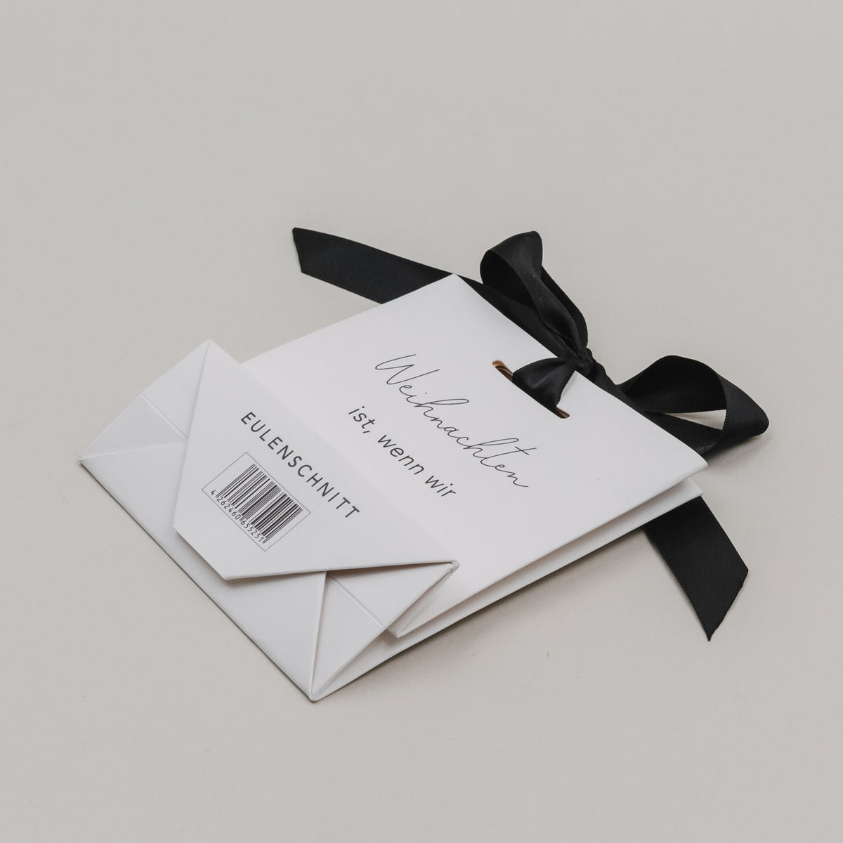 Gefaltete weiße Geschenktüten-Ansicht mit schwarzer Schleife, Text „Weihnachten ist, wenn wir zusammen sind.“