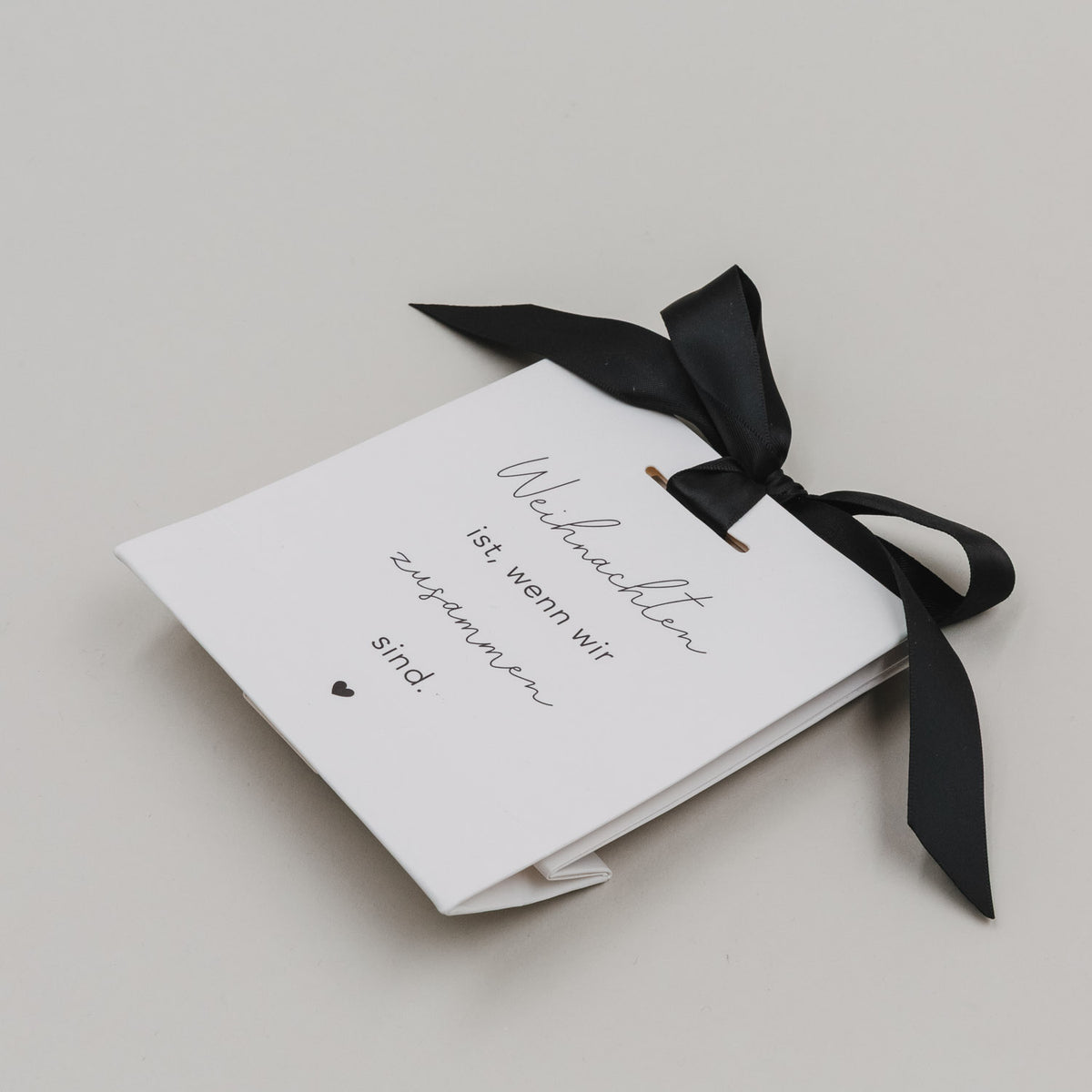 Übersicht zweier weißer Geschenktüten: schwarze Schleifen, Text „Weihnachten ist, wenn wir zusammen sind.“