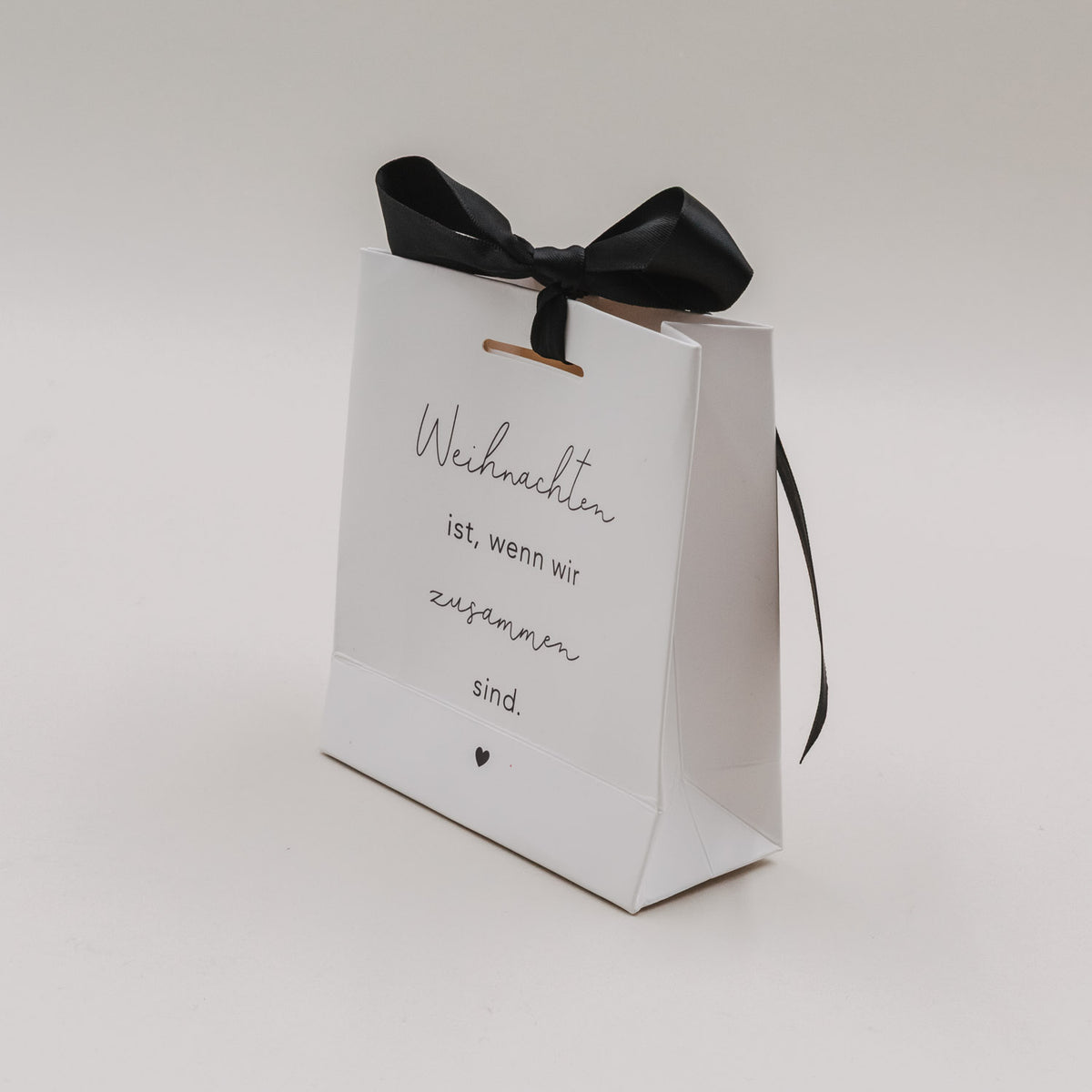 Weiße Mini-Geschenktüte mit schwarzer Schleife oben und Text „Weihnachten ist, wenn wir zusammen sind.“