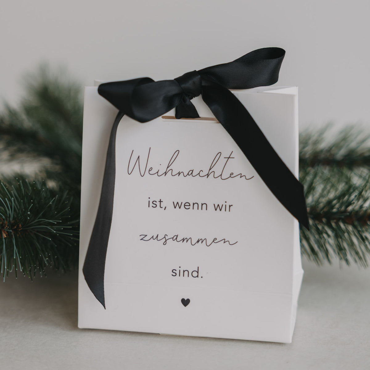 Weiße Geschenktüte mit schwarzem Schleifenband, Aufdruck „Weihnachten ist, wenn wir zusammen sind.“