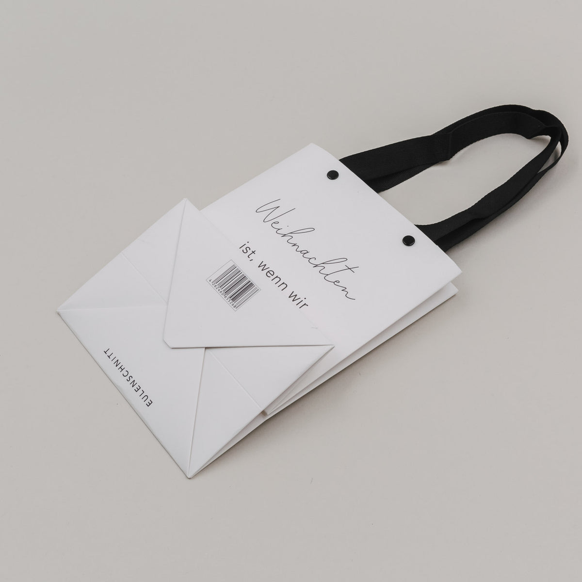 Weiße Geschenktüte mit schwarzen Griffbändern, Schriftzug und Barcode-Aufkleber