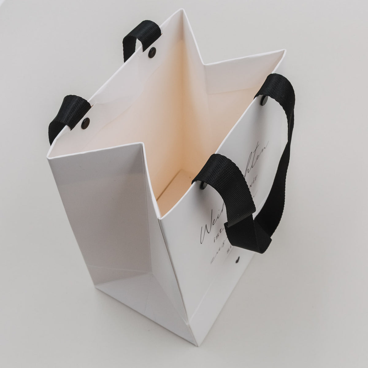 Weiße Geschenktüte geöffnet, mit schwarzen Griffbändern, innen sichtbar