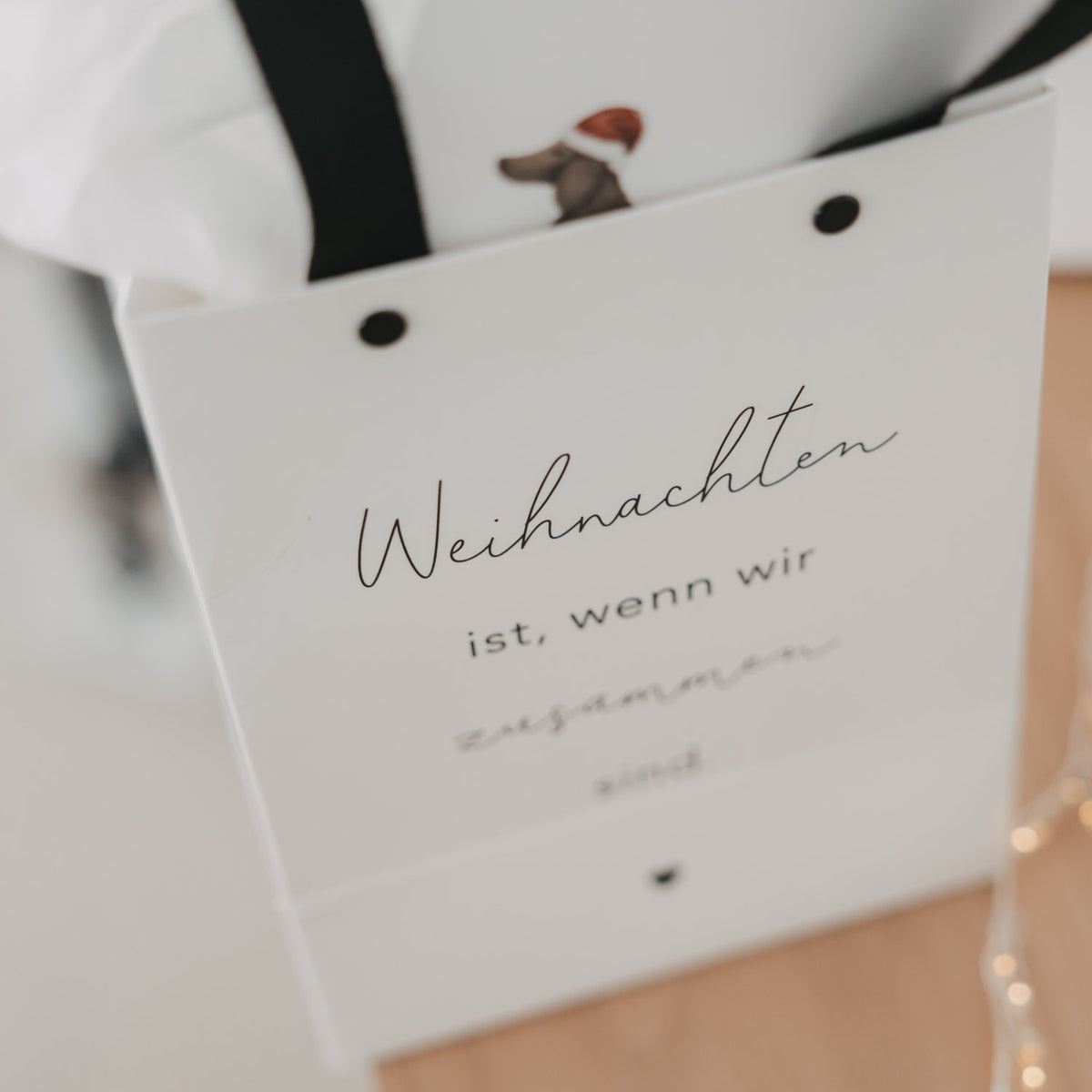 Weiße Geschenktüte schrägansicht mit schwarzem Trageband und Schriftzug „Weihnachten ist“