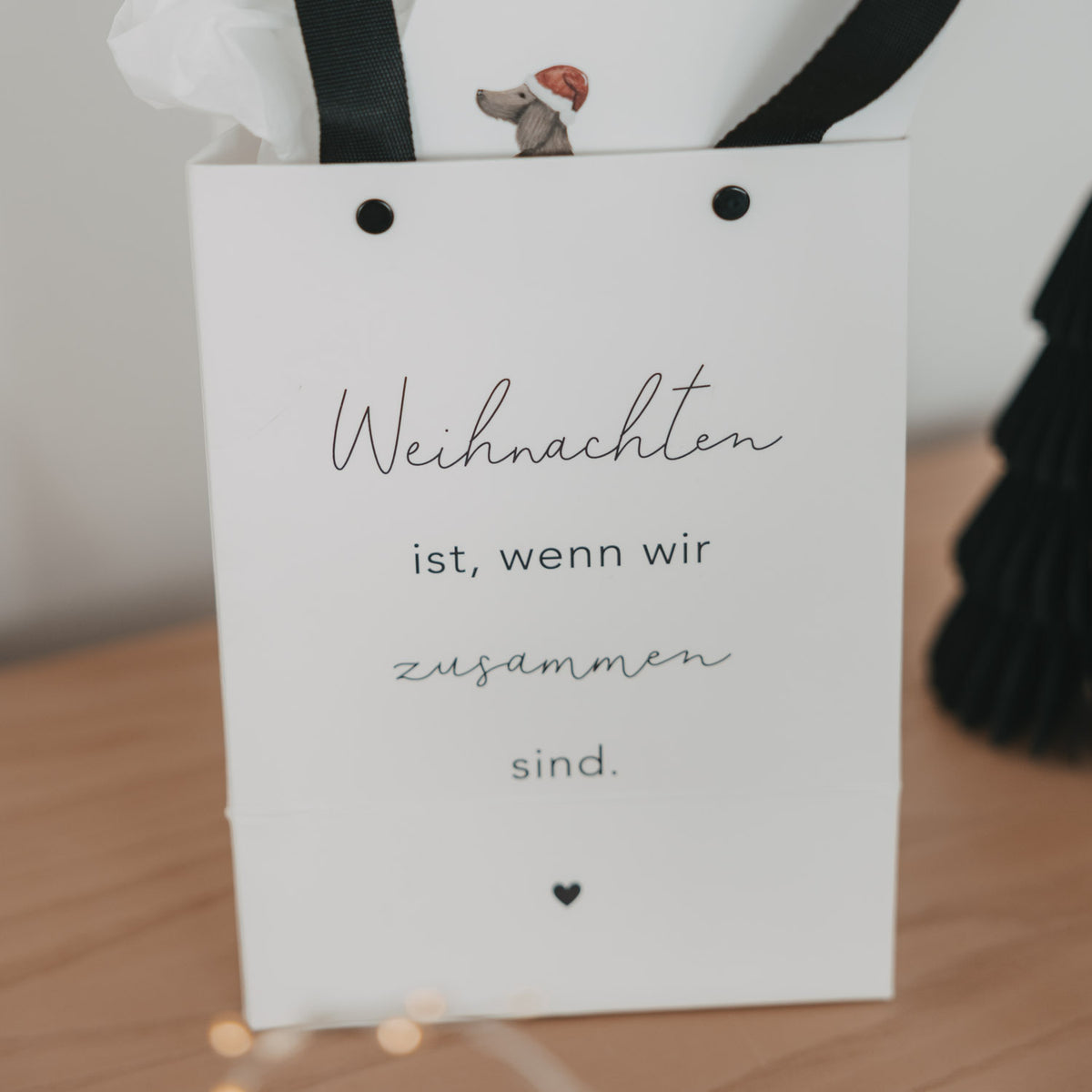 Weiße Geschenktüte mit schwarzen Tragebändern und Text „Weihnachten ist, wenn wir zusammen sind“