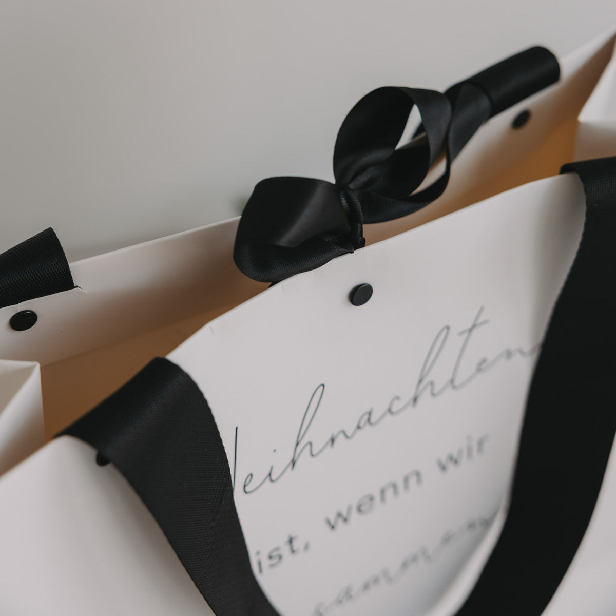 Nahaufnahme: weiße Geschenktüte mit schwarzer Schleife und Schriftzug „Weihnachten ist…“