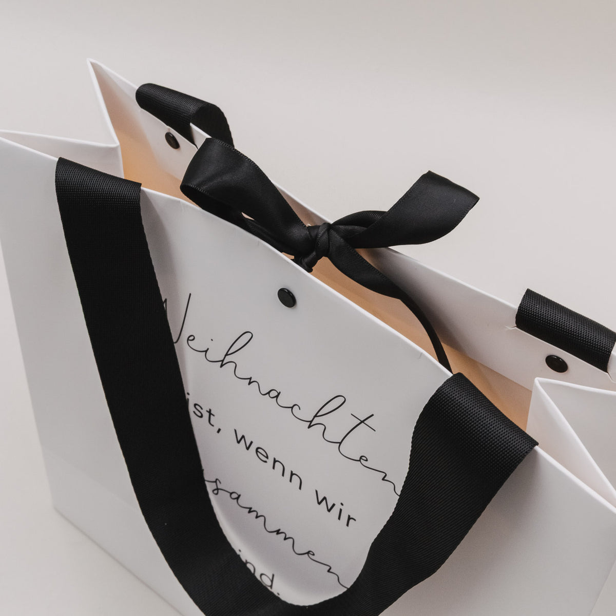 Weiße Geschenktüte mit schwarzem Band und Schriftzug „Weihnachten ist, wenn wir zusammen sind“