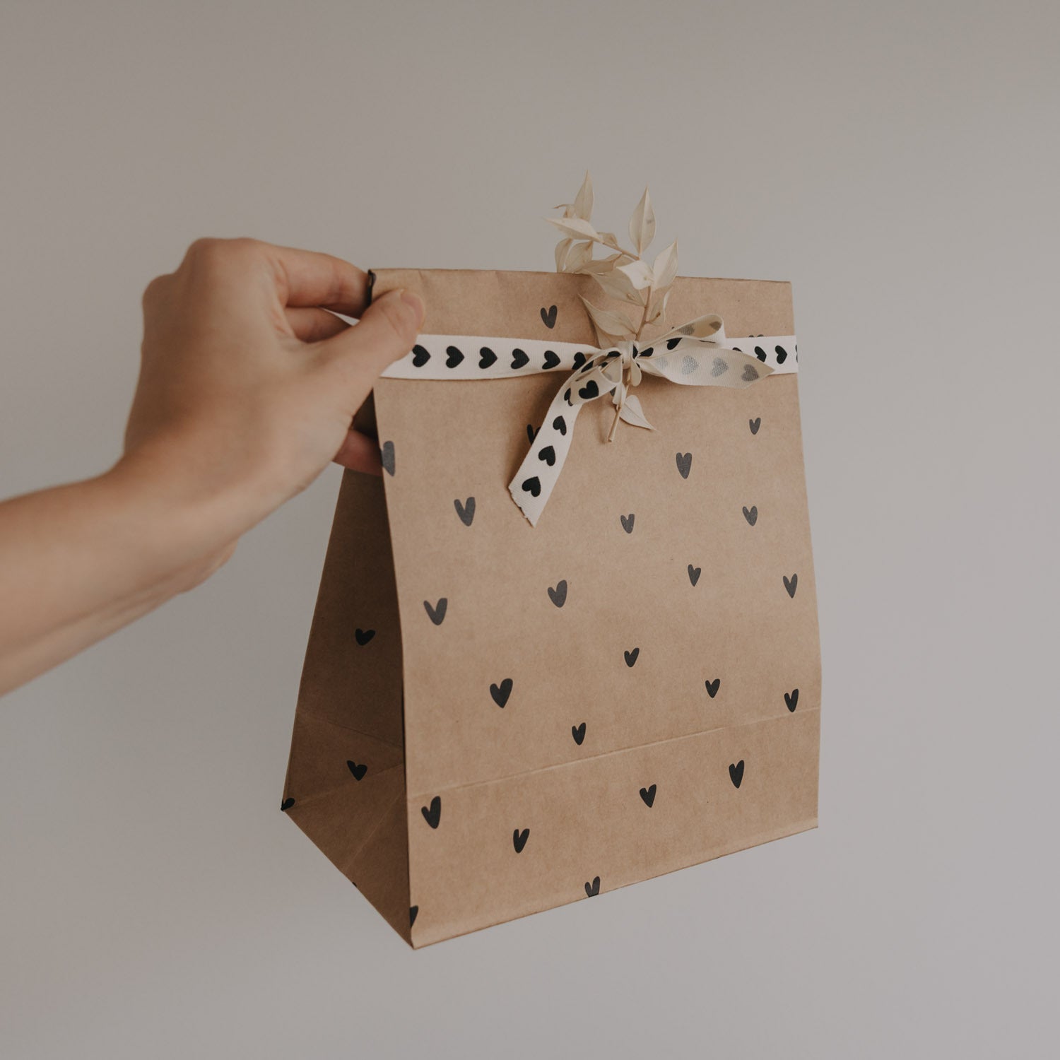 Herzbedruckte Papiertüte mit Schleife und Bandgriff, von Hand gehalten