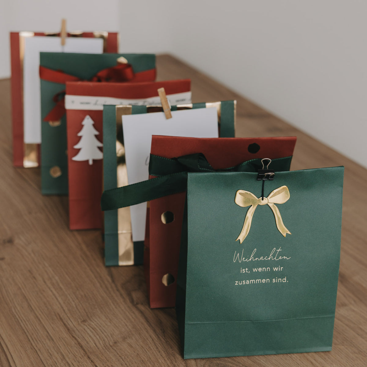 Grüne Papiertüte mit Schleife und Weihnachtsbaum-Illustration sowie Spruch