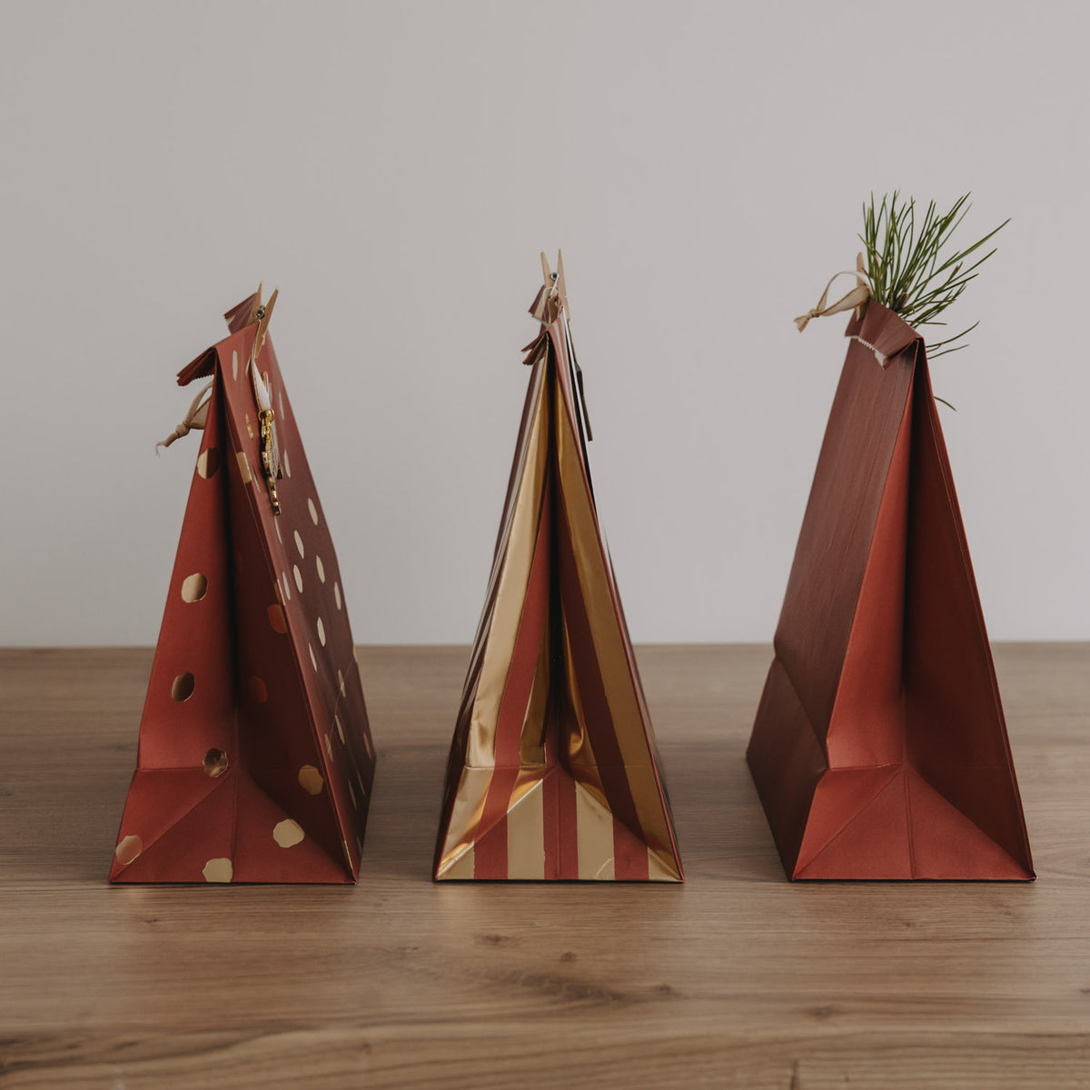 Drei Papiertüten in Rot/Braun mit Weihnachtsdekor, eine mit goldenen Punkten