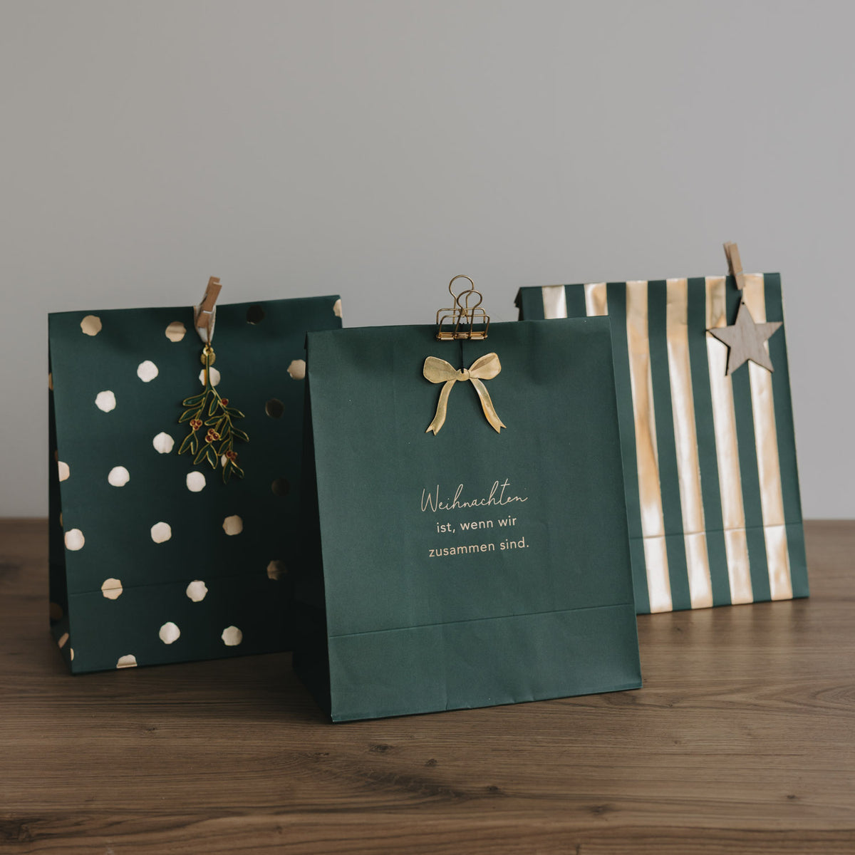 Mehrere weihnachtliche Papiertüten in Grün mit Schriftzug, Punkten und Streifen