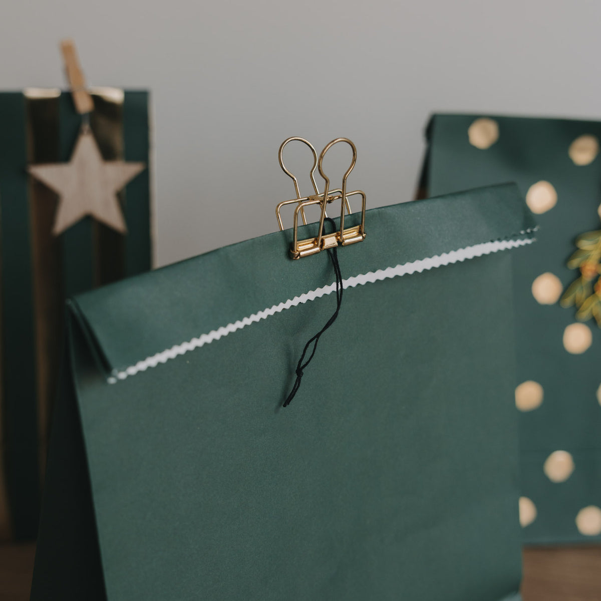 Dunkelgrüne Papiertüte mit Weihnachtsmotiv und Holzklammer, seitlicher Henkel