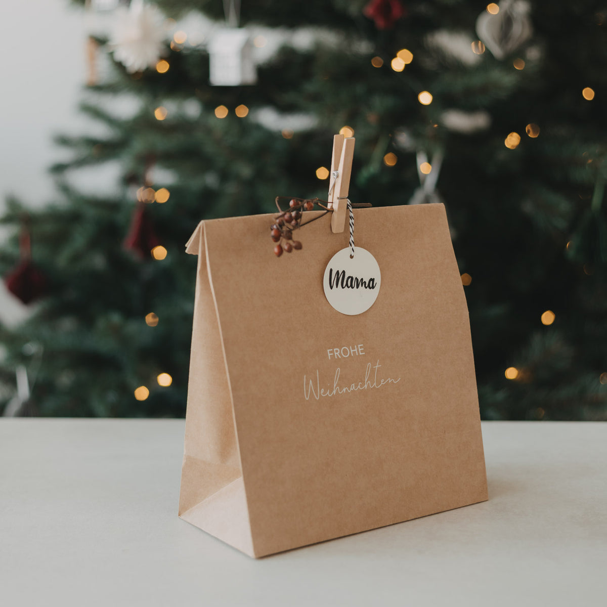 Braune Papiertüte mit Wäscheklammer-Anhänger „Mama“ und Schrift „Frohe Weihnachten“