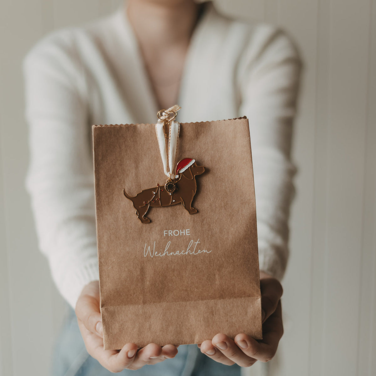 Braune Papiertüte mit „Frohe Weihnachten“ und Reh-Anhänger, in Hand gehalten