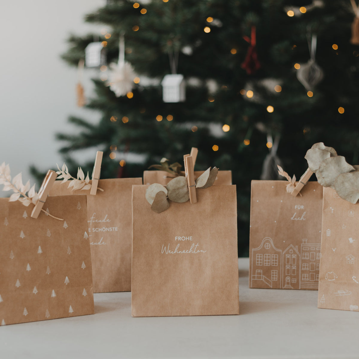 Papiertüten aus braunem Papier mit weißen Weihnachtsmotiven, aufgereiht auf dem Tisch