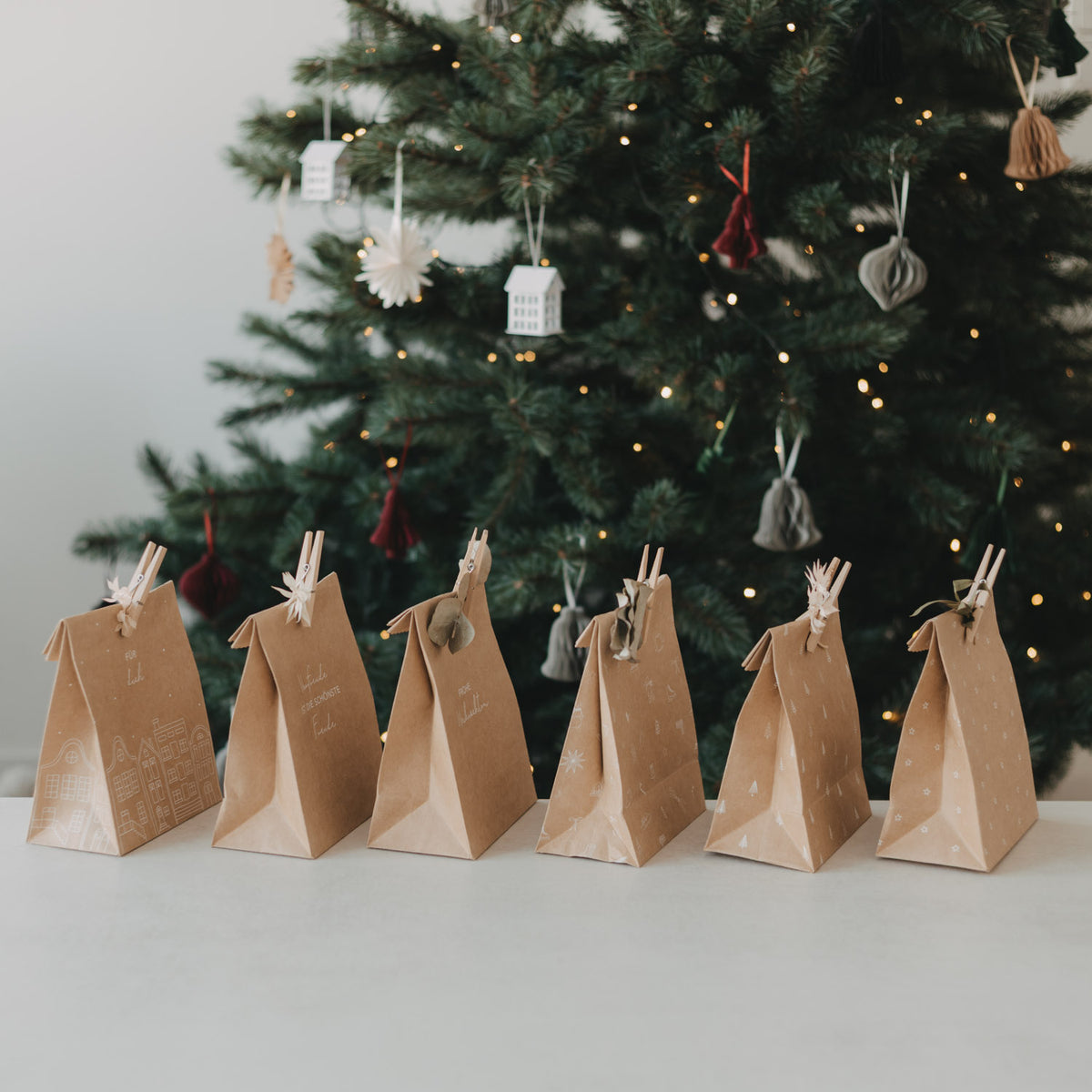 Mehrere braune Papiertüten mit Weihnachtsmotiven und Klammergriffen am Tannenbaum
