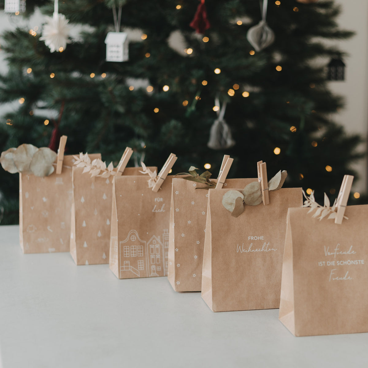 Mehrere braune Papiertüten mit Weihnachtsdruck, jeweils oben mit Klammergriff und Schleife