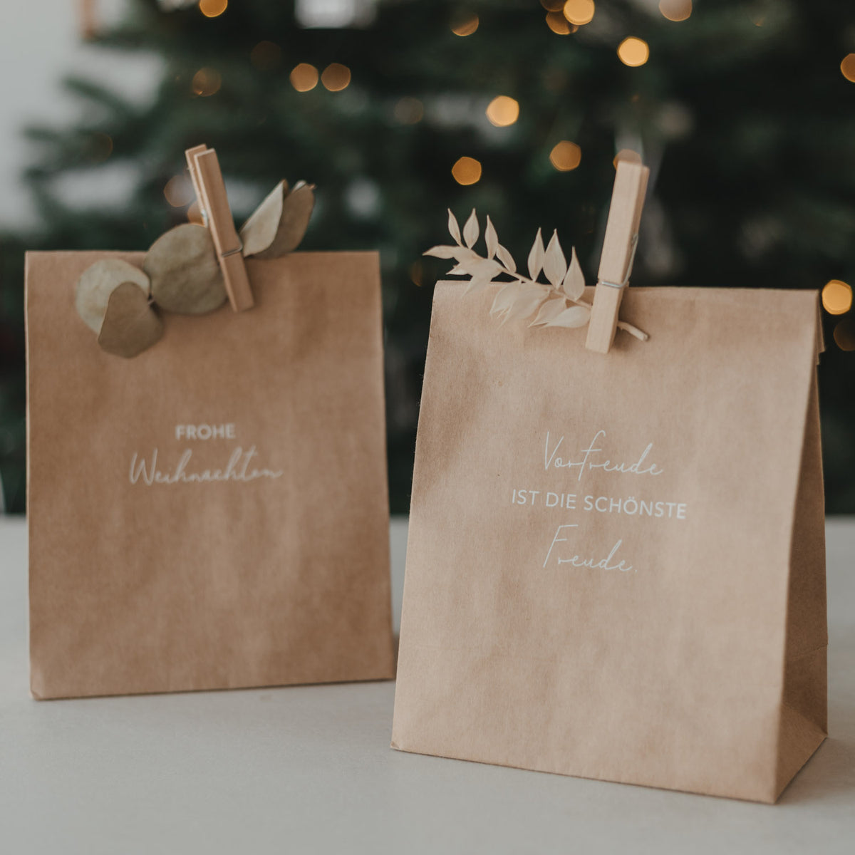 Zwei braune Papiertüten mit „Frohe Weihnachten“-Spruch, oben mit Stoffschleifen und Klammern
