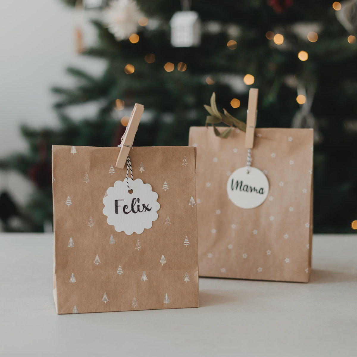 Braune Papiertüte mit Tannenmuster und Anhänger „Feliz“, oben mit Klammergriff
