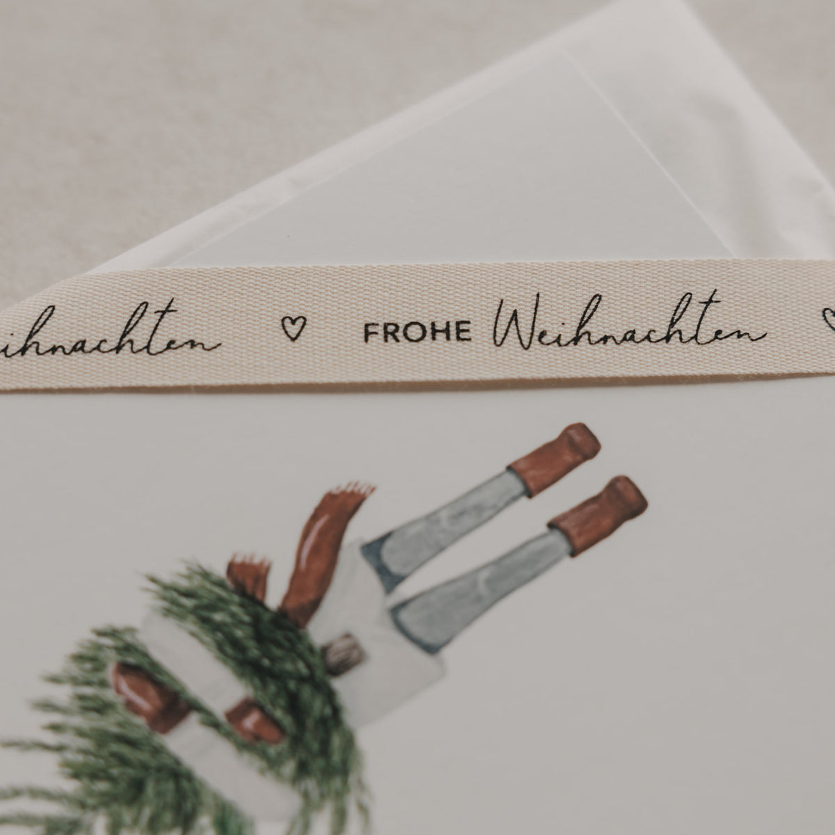 Geschenkband mit „FROHE WEIHNACHTEN“ und Weihnachtsillustration auf beiger Webstruktur